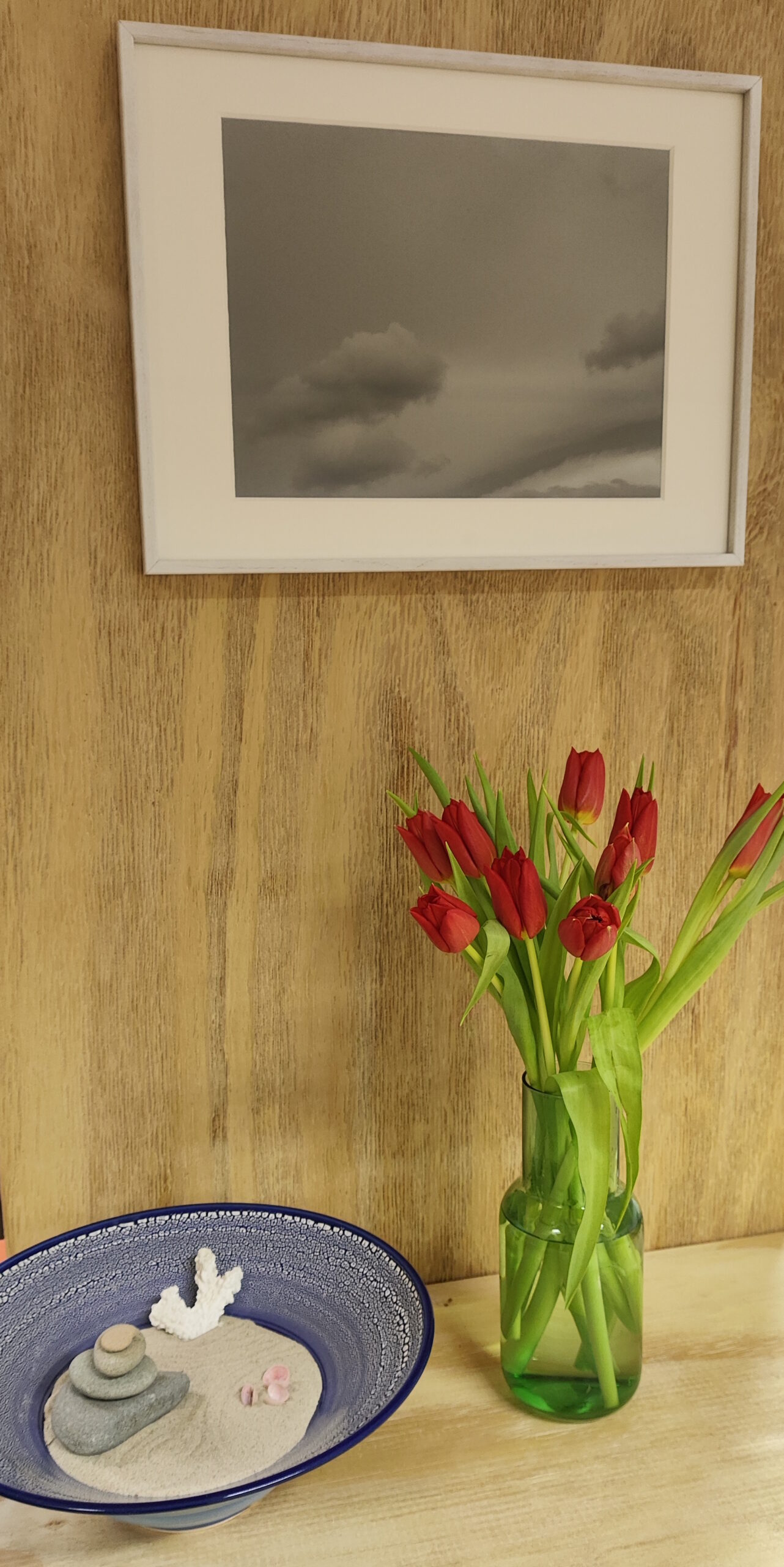 Einblick in die Praxisräume Eine Schale auf einem Holzregal. Daneben eine Vase mit roten Tulpen und darüber ein Bild