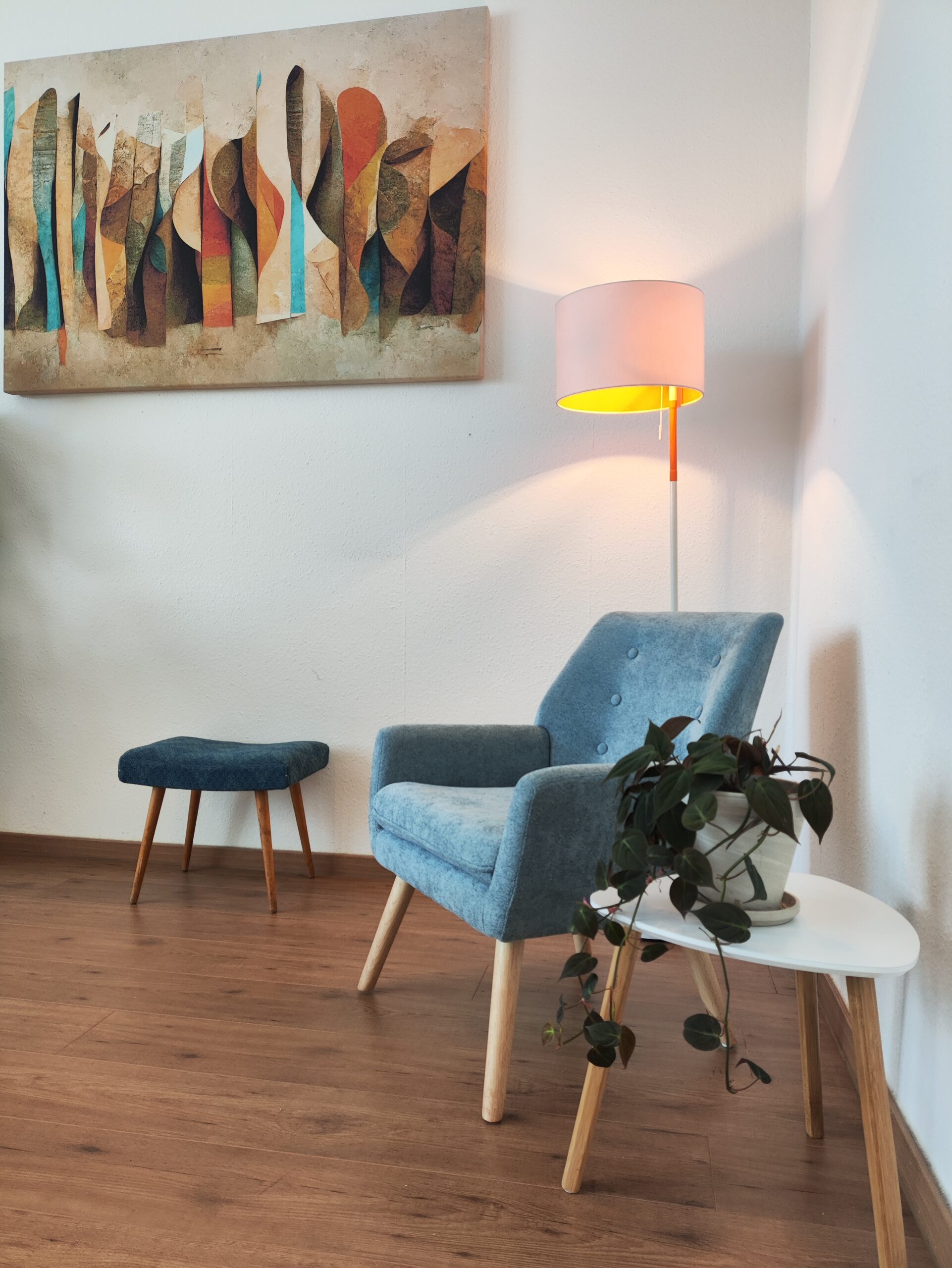 Einblick in die Praxisräume Ein Stuhl in einer gemütlichen Ecke mit einem Tisch daneben und einer Stehlampe dahinter. An der Wand hängt noch ein Bild