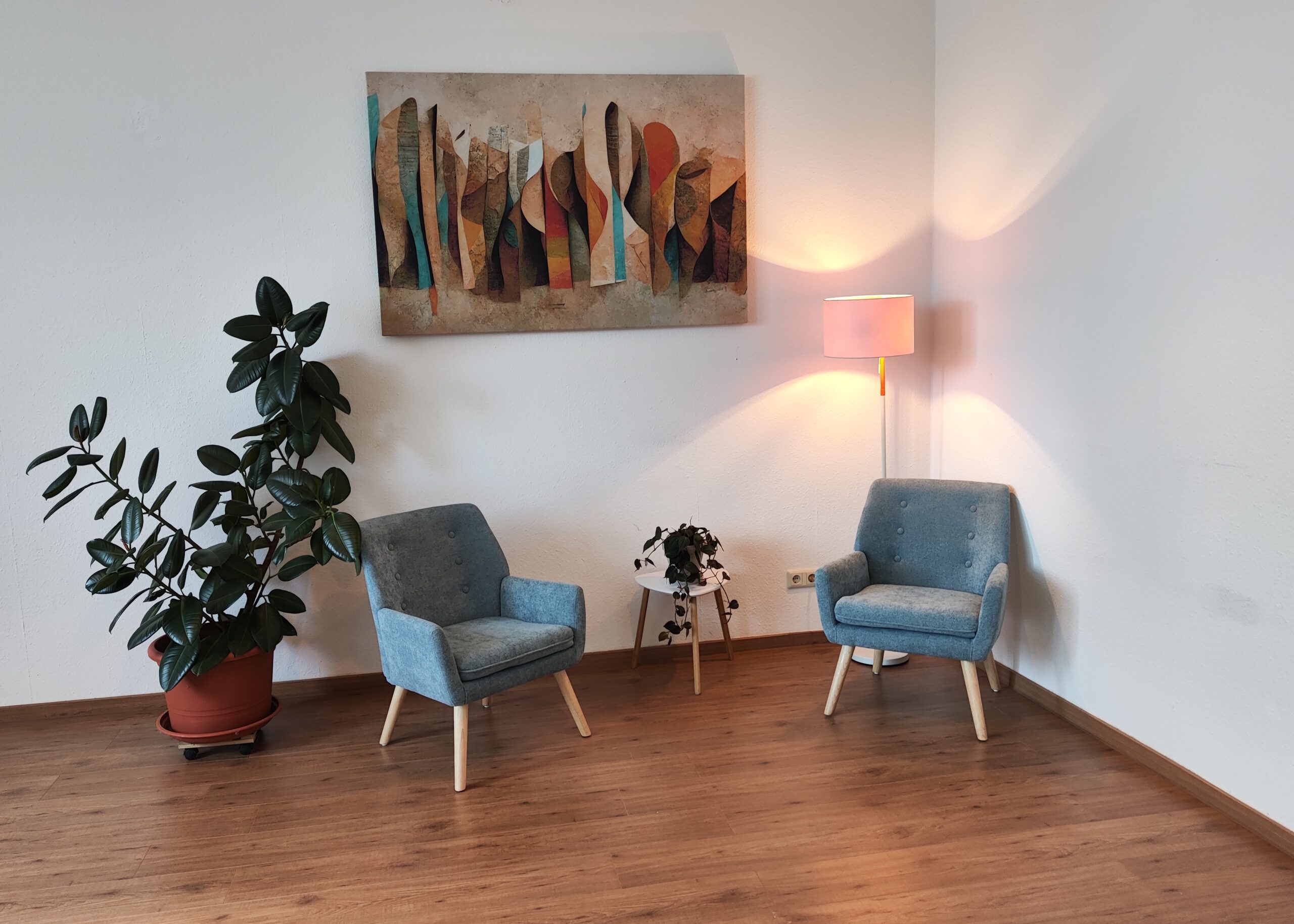 Räumlichkeiten Praxisräume Zwei gemütliche Stühle stehen in einer Ecke mit Licht, einem Bild und einer Pflanze.